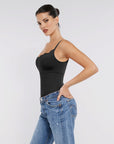 Woman wearing a black bodysuit and blue jeans against a plain background.