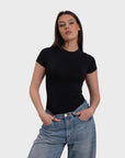 A woman wearing a short sleeve crew neck black bodysuit and blue jeans.