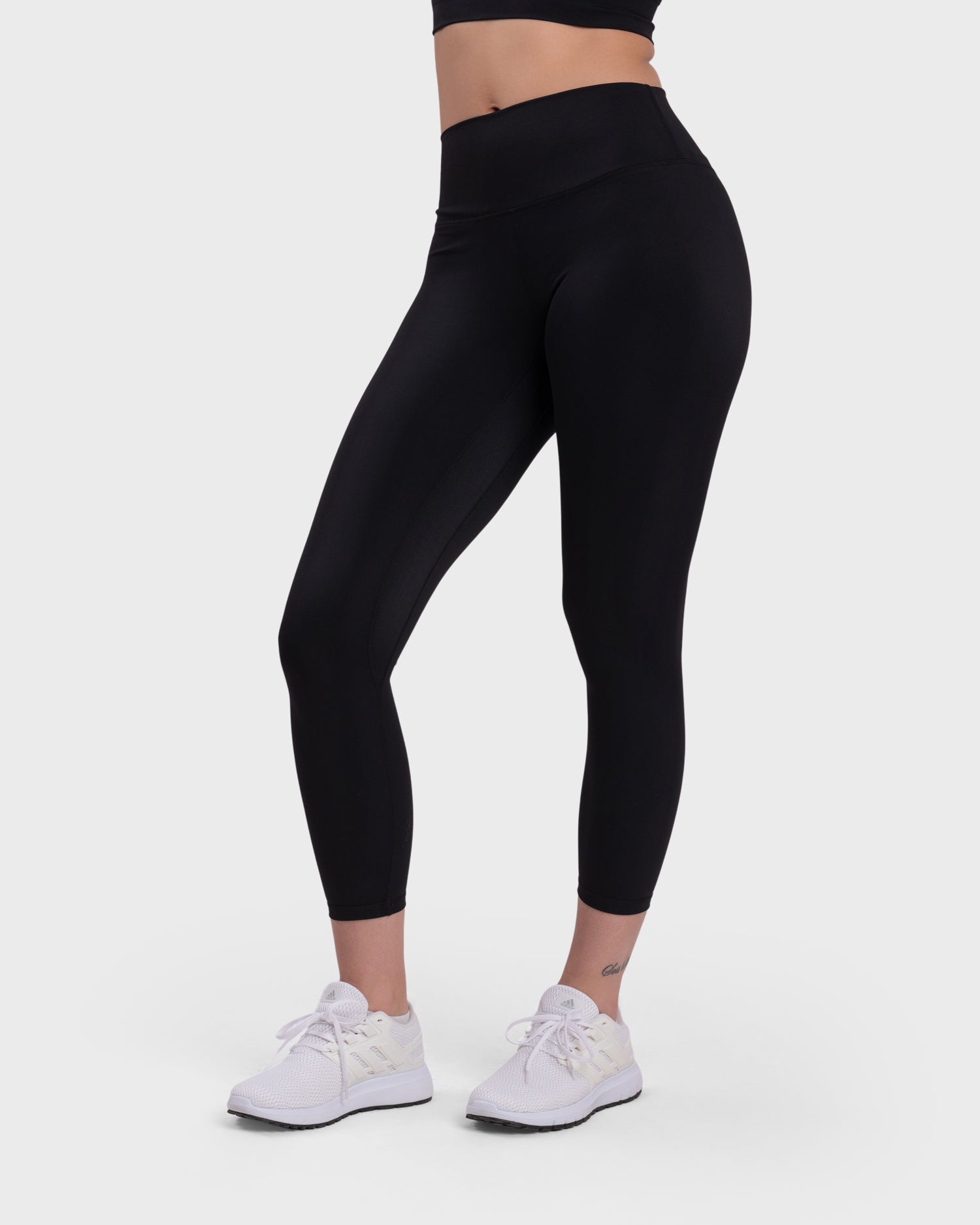 A female model wearing black active leggings and white sneakers.